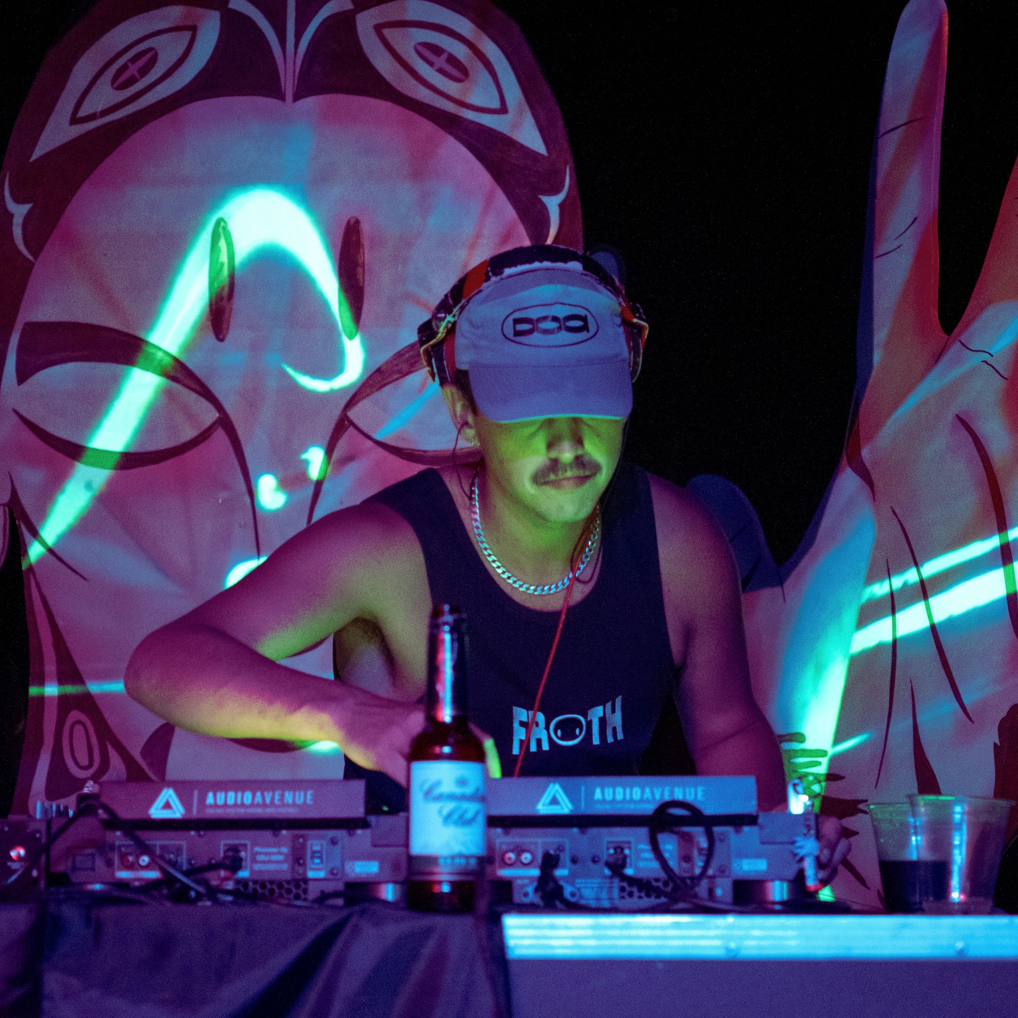 A DJ leaning over the decks, face half hidden, waving lines of light crossing the backdrop behind them